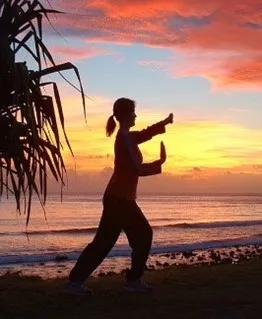 woman doing qigong poses in front of sunrise